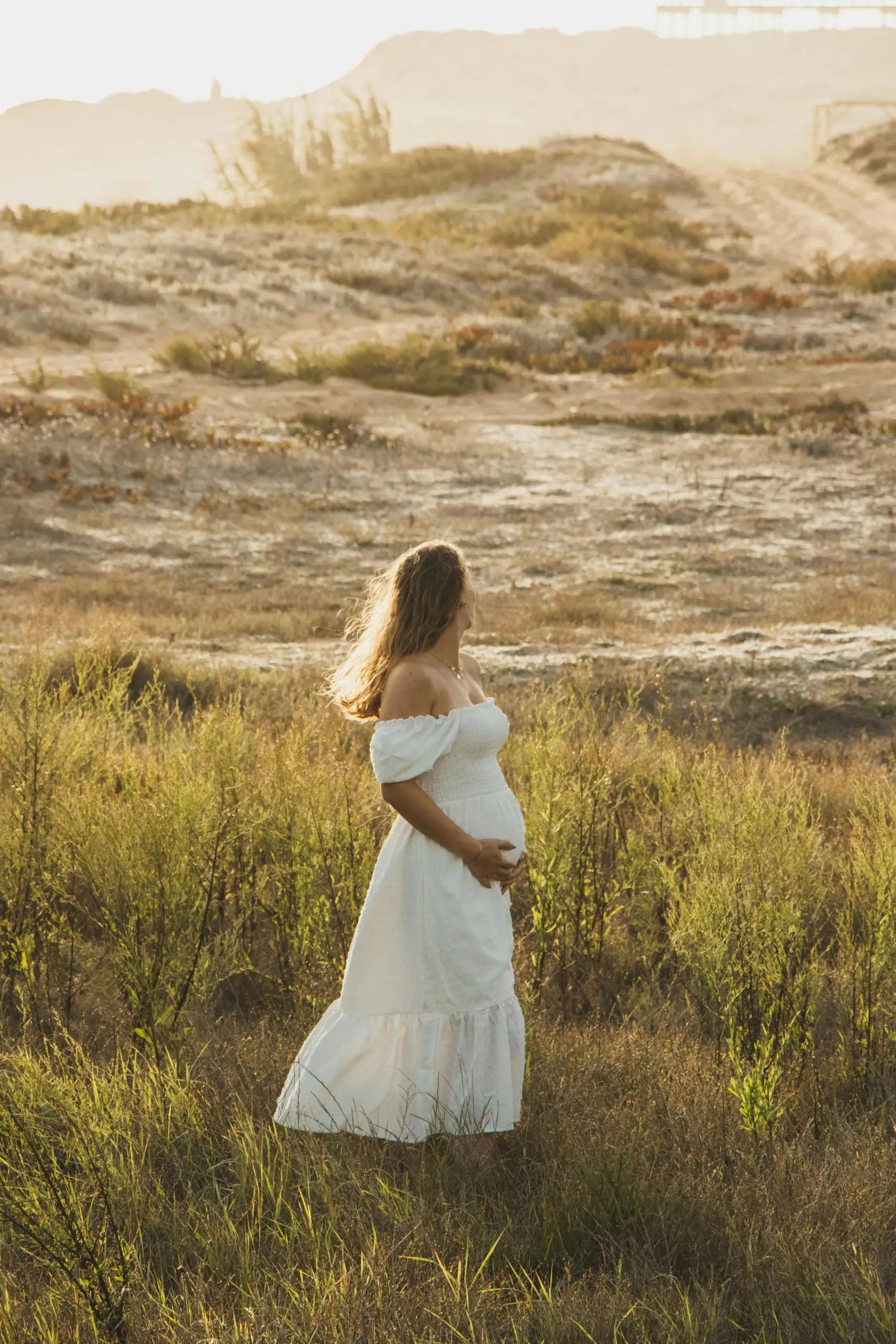 Pregnant woman in white dress enjoying a beautiful outdoor summer scene.